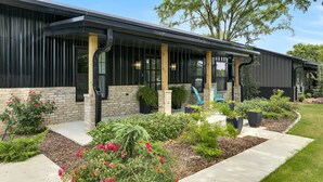 Un bâtiment moderne avec une façade en briques, de grandes fenêtres et un espace porche couvert doté de sièges extérieurs.