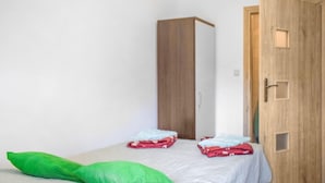 Ein kleiner, schlichter Raum mit einem Bett, einem grünen Kopfkissen und einem hölzernen Kleiderschrank.