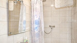 Ein Badezimmer mit Dusche, einem gläsernen Spiegel, einem Waschbecken mit Seifenspender und einem Handtuch an der Wand.