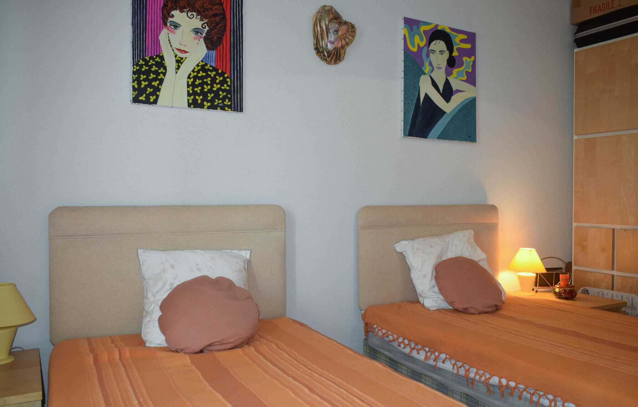 Deux lits avec des têtes de lit, une lampe et deux tableaux accrochés au mur.