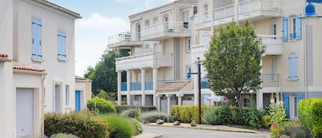 A residential street with multi-story buildings, balconies, and well-maintained gardens.