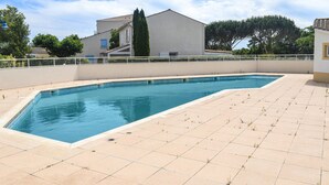 Una piscina rettangolare con bordo piastrellato, circondata da un basso recinto bianco, con edifici sullo sfondo.