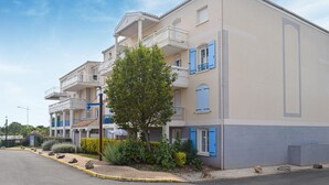 Un edificio residenziale a più piani con balconi, un albero nel cortile e cielo sereno.