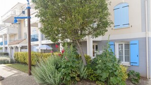 Una serie di edifici residenziali con persiane blu e un’area giardino con diverse piante e un albero.