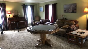 A living room with a round coffee table, a piano, a sofa, and a lamp. - EAA house on golf course (Oshkosh)
