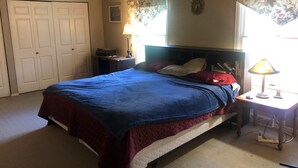 A bedroom with a bed, a nightstand, a lamp, a desk, and a window with curtains. - EAA house on golf course (Oshkosh)