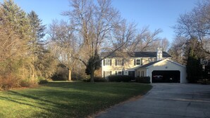 A two-story house with a garage, surrounded by trees and a well-maintained lawn. - EAA house on golf course (Oshkosh)