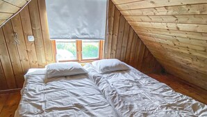 Ett sovrum med ett sluttande tak av trä, en säng med vitt sänglinne och ett fönster med utsikt över grönskan utanför.