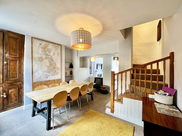A dining area with a long wooden table and chairs, a hanging light fixture, and a staircase with wooden railings. - Cathedral Quarter - sleeps 8 (Lincoln)