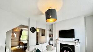 En stue med en hvid sofa, et træbord, en pejs, et tv ophængt over pejsen og en reol med bøger.