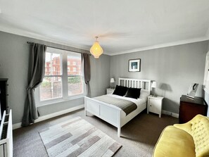 A bedroom with a bed, bedside tables, a lamp, a chair, a window with curtains, and a picture on the wall. - Cathedral Quarter - sleeps 8 (Lincoln)