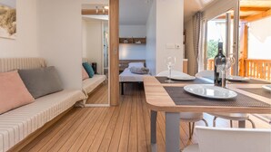 Een knus ingerichte kamer met een bed, een bank, een eettafel met stoelen en een balkon met houten spijlen.