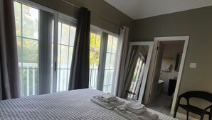A hotel room with a large bed, a view of the outdoors through the windows, and a door leading to a bathroom. - Family friendly Townhouse by the Bay , private Beach & Pool , Negril  (Negril)