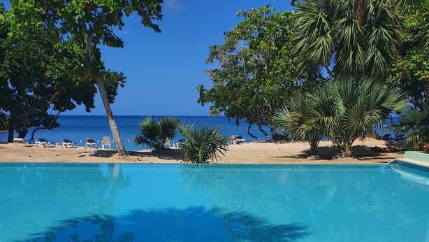 A person relaxing on a lounge chair by a pool with a view of the ocean. - Family friendly Townhouse by the Bay , private Beach & Pool , Negril  (Negril)