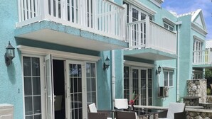 A two-story house with a balcony, outdoor seating area, and a stone wall. - Family friendly Townhouse by the Bay , private Beach & Pool , Negril  (Negril)