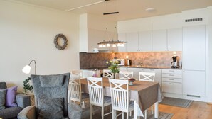 Una cocina moderna con armarios blancos, una zona de comedor con mesa y sillas, y un sillón gris.