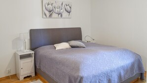 Un dormitorio con una cama, una mesita de noche, una lámpara y una obra de arte colgada en la pared.