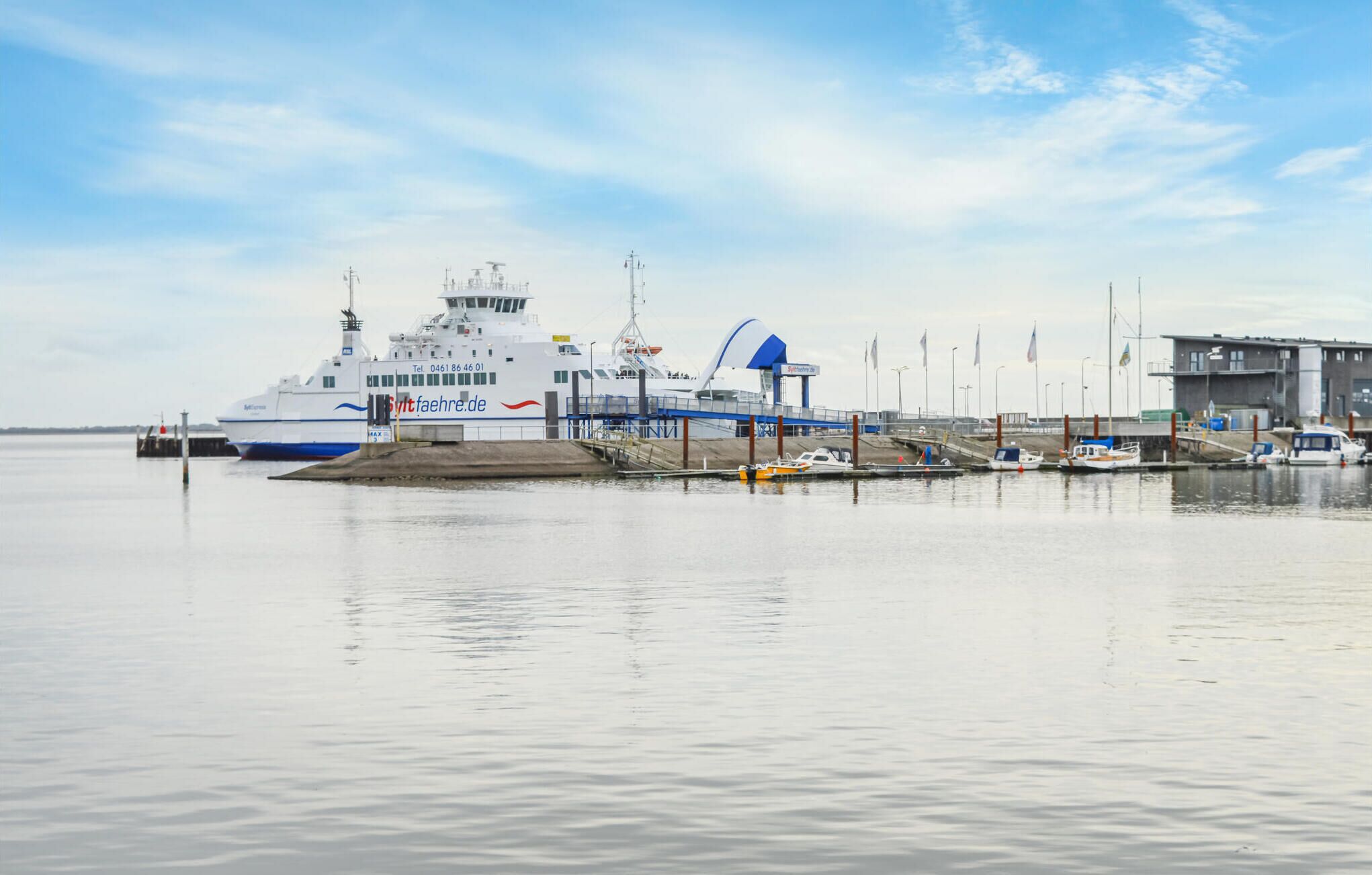 Un ferry était amarré à un quai, avec un petit bateau au premier plan et un bâtiment en arrière-plan.