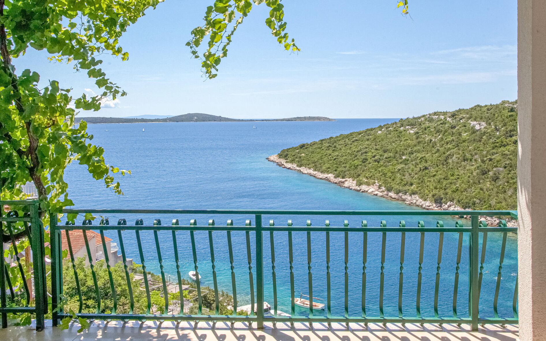 Un balcon offrant une vue sur une zone côtière, avec une mer bleue et limpide et un paysage vallonné.