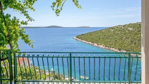 A balcony with a view of a coastal area, including a clear blue sea and a hilly landscape.