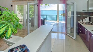 A modern kitchen with a gas stove, a dining area with a white table, and a view of the sea through a glass door.