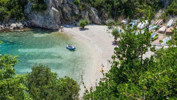 A beach with clear water, a boat, and a rocky cliff.