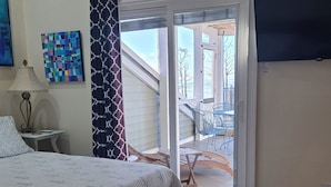 Une chambre à coucher avec un lit, un ventilateur de plafond, une fenêtre avec des rideaux, un tableau et une vue sur l’extérieur.