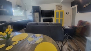 Un salon moderne avec un canapé gris, un meuble jaune et un téléviseur à écran plat.