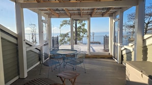 Un espace extérieur abrité, doté d’une terrasse en bois, de chaises en métal et d’une table.