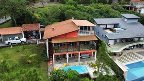 A multi-story house with a large balcony, a swimming pool, and a car parked nearby.