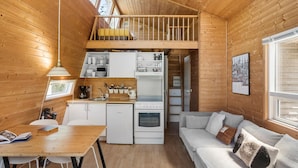 A cozy cabin with a loft bedroom, a kitchenette, and a living area with a sofa and a dining table.