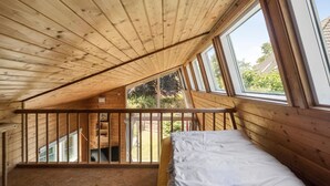 A bedroom with a sloped ceiling, wooden beams, a bunk bed, and large windows offering a view of the outdoors.