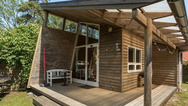 A wooden deck with a bench and a table, a sliding glass door, and a small window.