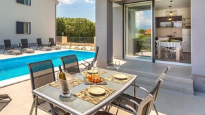 A poolside dining area with a table set for two, a bottle of wine, and a glass of water. - Awesome apartment in Vrbnik with WiFi (Vrbnik)