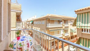 Un balcón con una mesa dispuesta para dos, con vista a una calle con edificios.