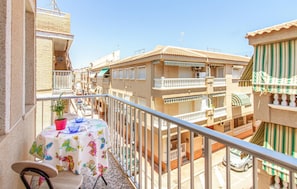 A balcony with a table set for two, overlooking a street with buildings.
