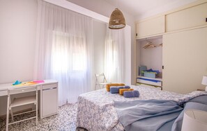 A bedroom with a bed, a desk, a chair, a wardrobe, and a hanging light fixture.