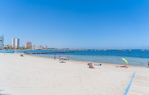 Ein Strand mit blauem Himmel, ruhiger See und Gebäuden im Hintergrund.