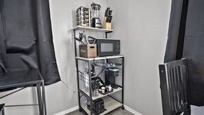 Une petite cuisine d’angle équipée d’un four à micro-ondes, d’une machine à café et d’étagères de rangement.