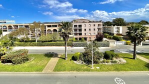 Un edificio de varios pisos con balcones, rodeado de vegetación cuidada y un cielo azul despejado.