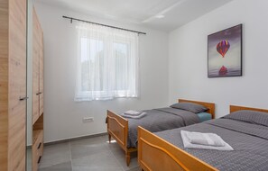 A bedroom with two beds, a window with sheer curtains, a painting of a hot air balloon, and a wooden wardrobe. - Beautiful apartment in Vrbnik (Vrbnik)
