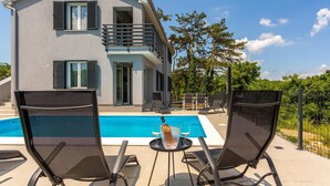 Ett modernt hus i två våningar med pool, utomhusmöbler och en balkong.