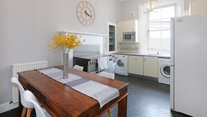 A compact kitchen with a dining area, including a wooden table, chairs, a vase with flowers, a clock, and modern appliances like a microwave and washing machine. - A fabulous 2-bedroom apartment in the heart of Edinburgh (Edinburgh)
