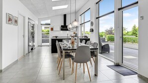 A modern kitchen with a dining area, large windows, and a view of greenery.
