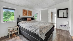 A bedroom with a large bed, two windows, a ceiling light, and a door leading to another room.