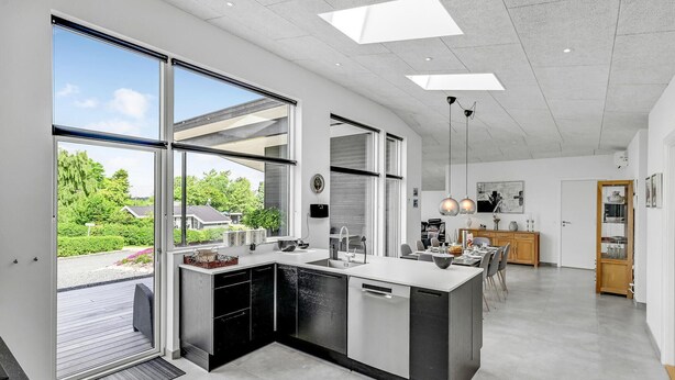 A modern kitchen with large windows, a central island, and a dining area with a view of the garden.