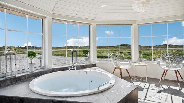 A modern bathroom with a large bathtub, large windows, and a view of the countryside. - Beautiful home in Ringkøbing with sauna (Ringkøbing)