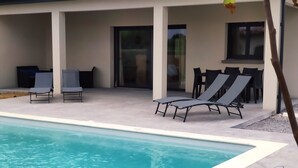 Una piscina con sillas de descanso y un porche cubierto.