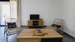 Una sala de estar moderna con mobiliario de mimbre, una mesa de centro de madera y un televisor de pantalla plana sobre un mueble de madera.