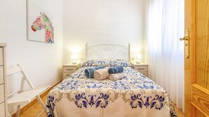 A neatly made bed with a patterned bedspread, two bedside lamps, a wall-mounted artwork, and a wooden door. - Gorgeous apartment in San Javier (San Javier)